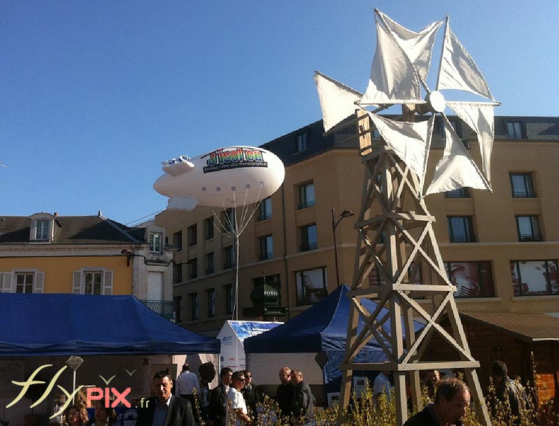 Ballon publicitaire en forme de dirigeable (zeppelin) avec marquage de logo personnalisé, ici utilisé pour l'animation d'un stand pendant un marché ou une foire.